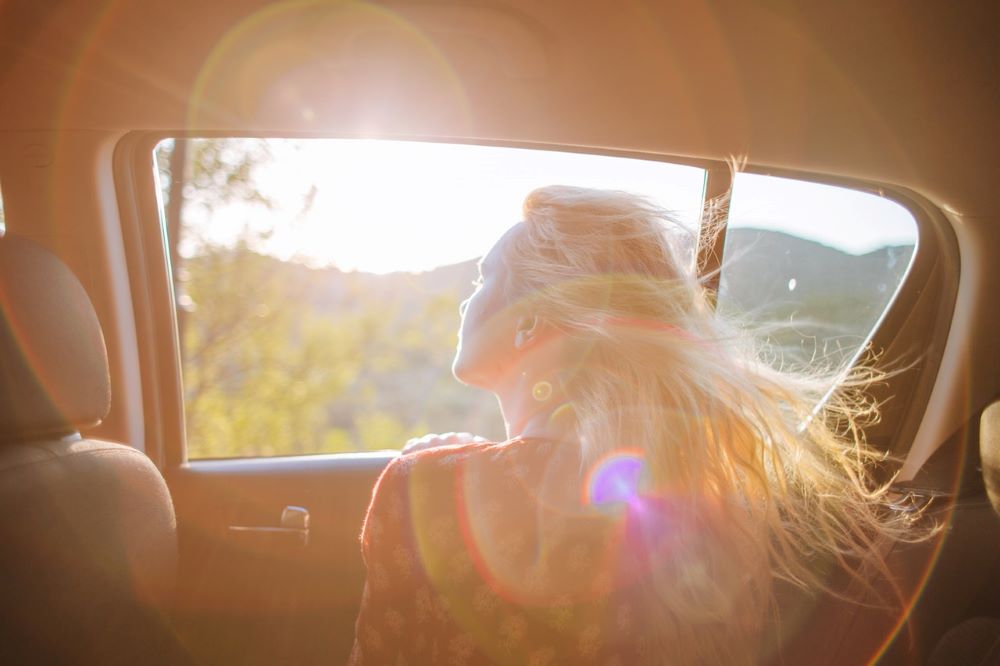 girl with head out the window of a car