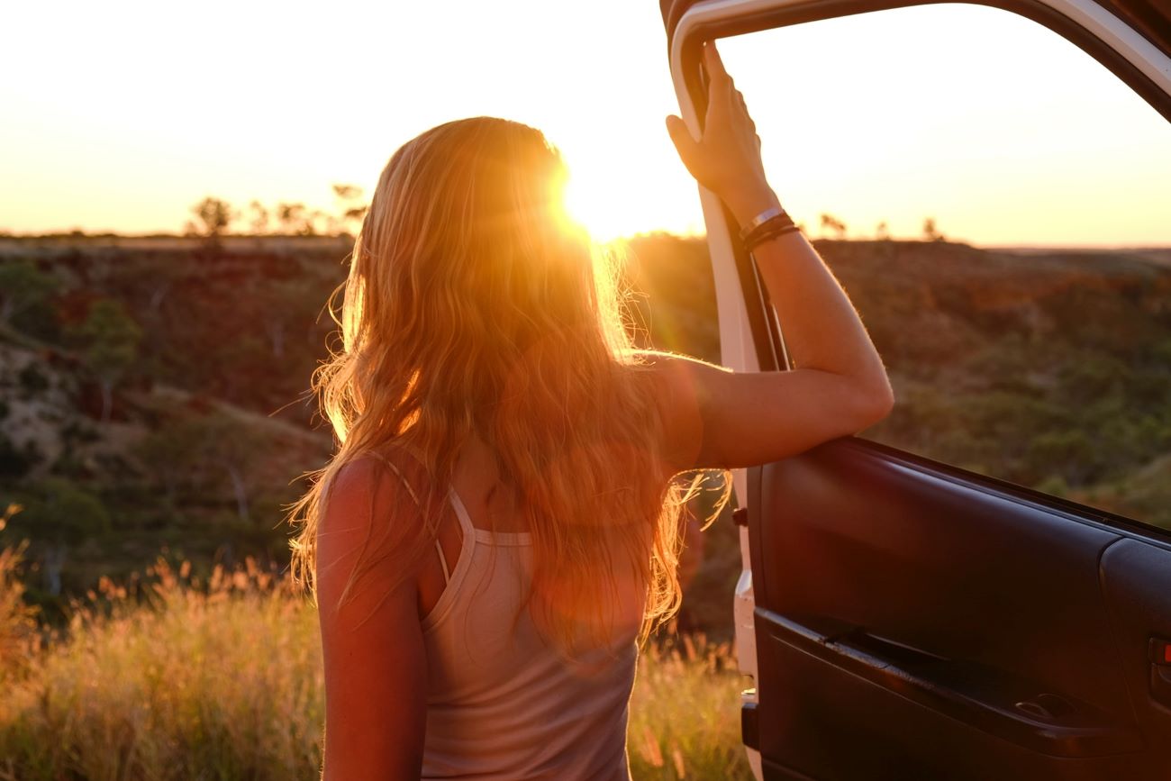 girl with car door in front of the setting sun