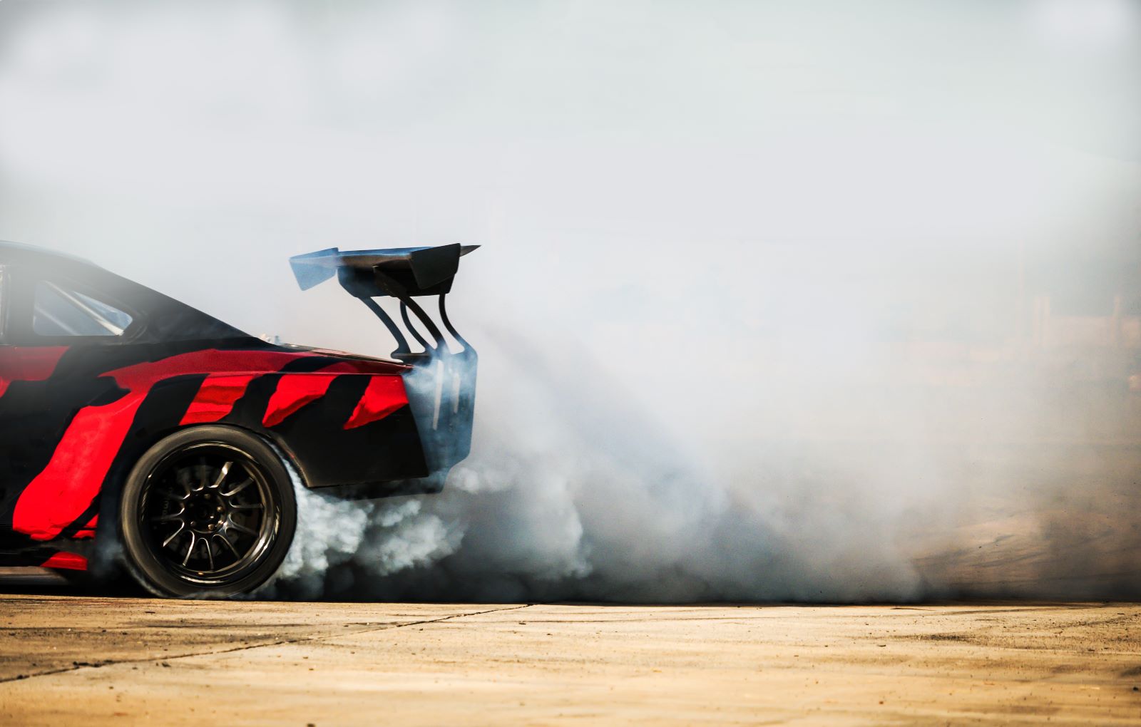 A black and red racecar spins tires in a cloud of smoke.