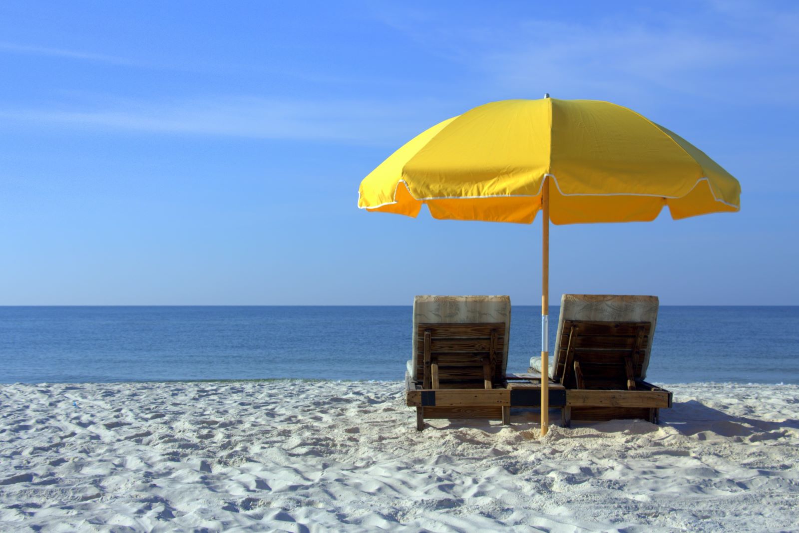 Two beach chairs under an umbrella facing the ocean on the beach.